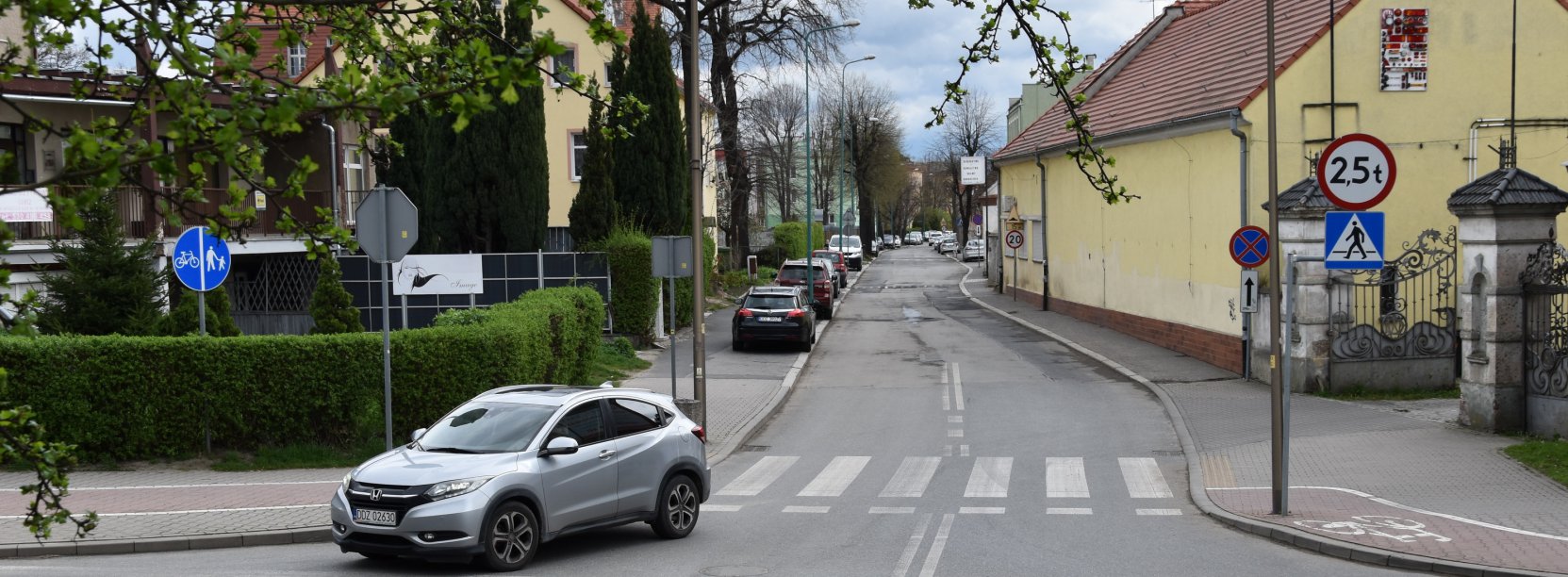 Skrzyżownie dróg, samochód włączający się do ruchu, po bokach zieleń i budynki