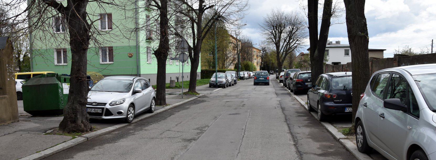 Droga asfaltowa, na chodnikach zaparkowane samochody