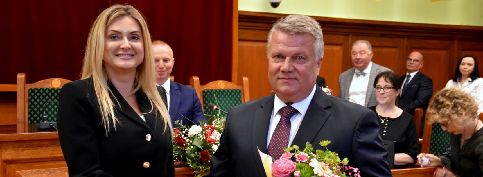 Uśmiechnięta kobieta, obok mężczyzna z bukietem kwiatów