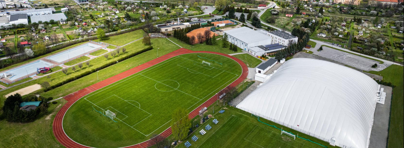 Boiska i hale sportowe widzine z głóry w drugim planie odkryte baseny io panorama miasta