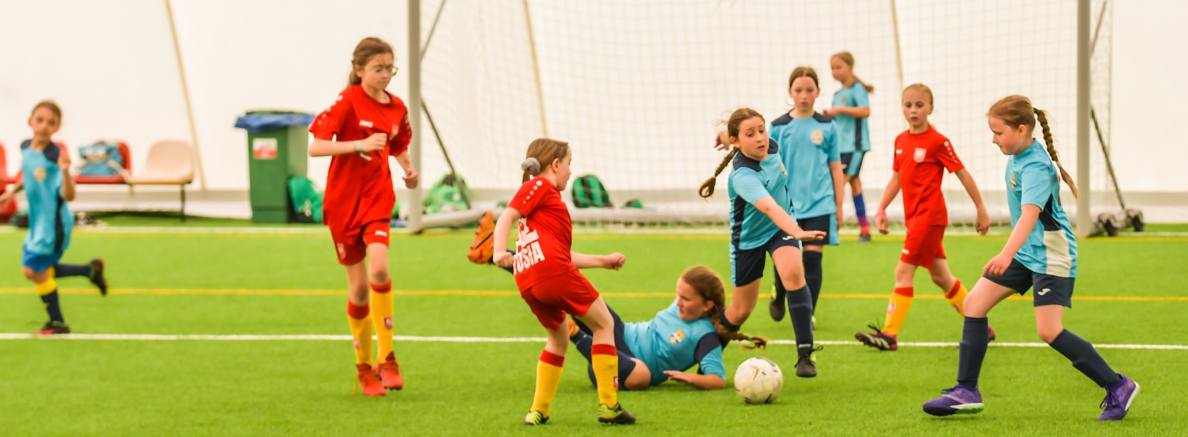 Młode dziewczyny w sportowych strojach grają w piłkę, w tle bramka