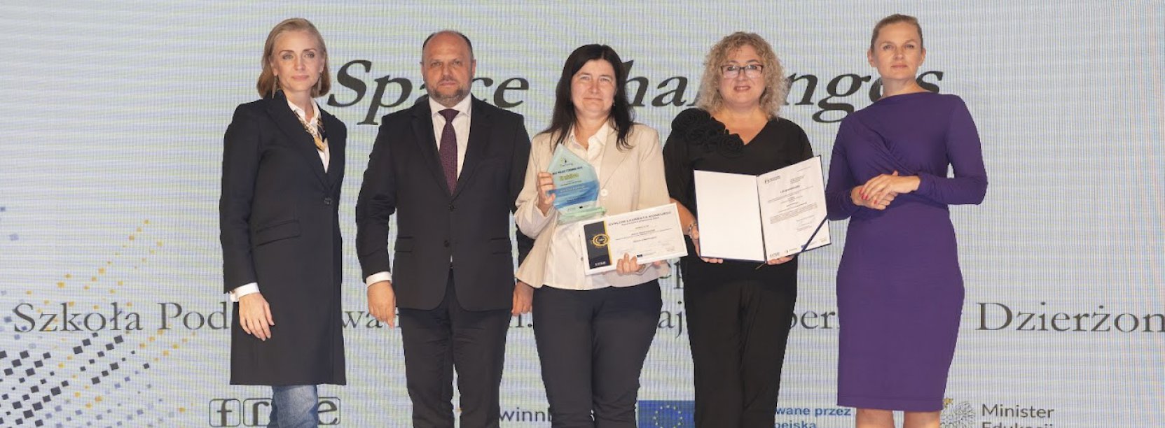 Cztery kobiety i mężczyzna pozują do wspólnej fotografii, za nimi jedolite tło