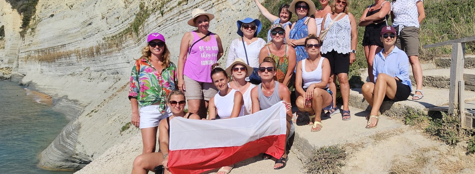 Grupa kobiet na kamenistej plaży, jedna z pań trzyma flagę Polski