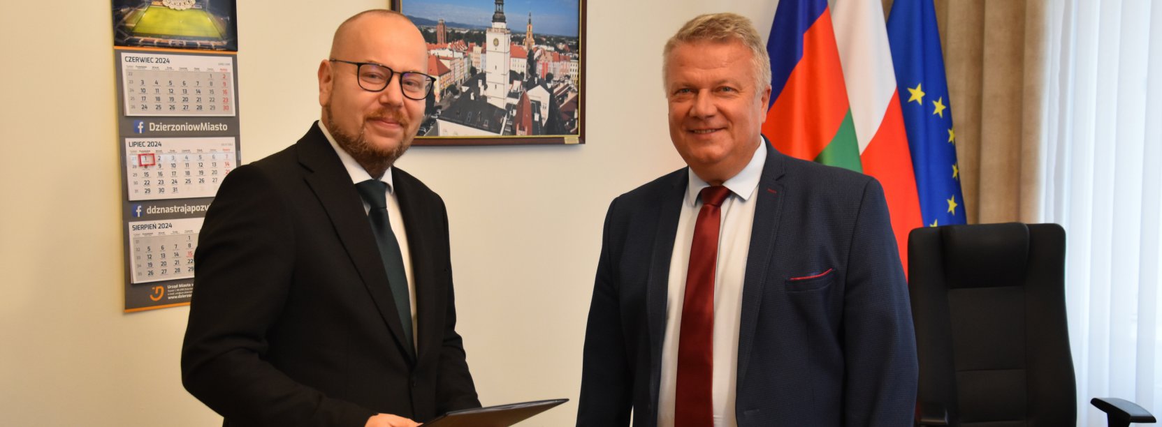 Zastępca odbierający nominację od burmistrza, gabinet, na ścianie obraz, obok flagi Dzierżoniowa, Polski i Unii Europejskiej