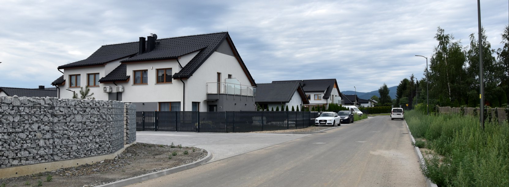 Ulica na osiedlu domków jednorodzinnych, Duży, biały dom, obok kamienny mur