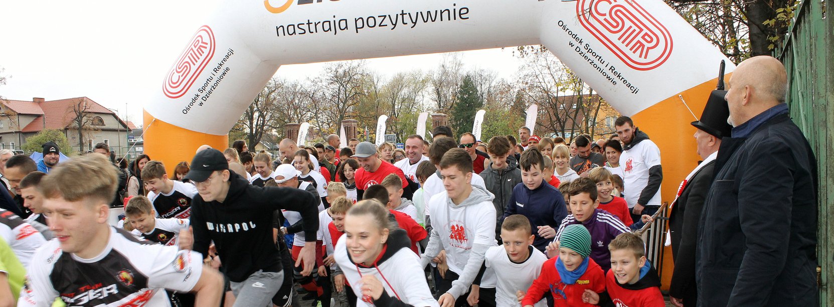 Tłum uczestników przebiega przez dmuchaną bramę startową, na niej napis Dizerżoniów nastraja pozytywnie