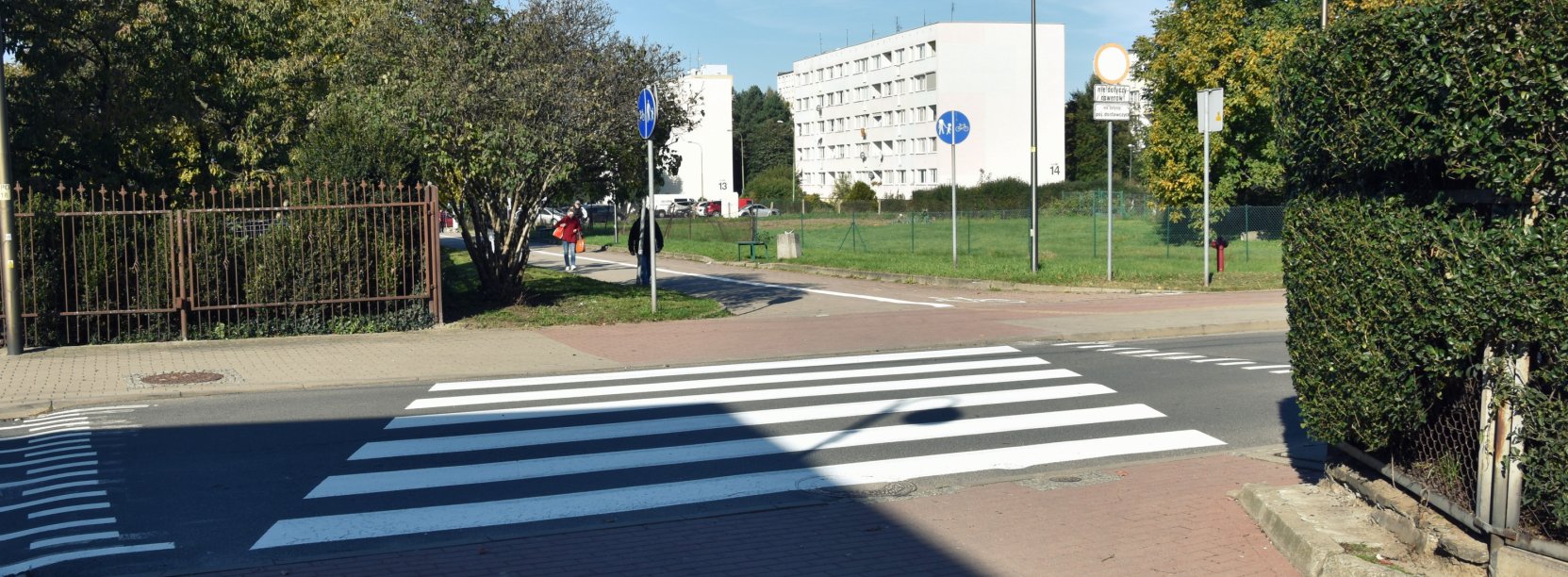 Przejście dla pieszych na drodze prowadącej na osiedle, w tle bloki mieszkalne