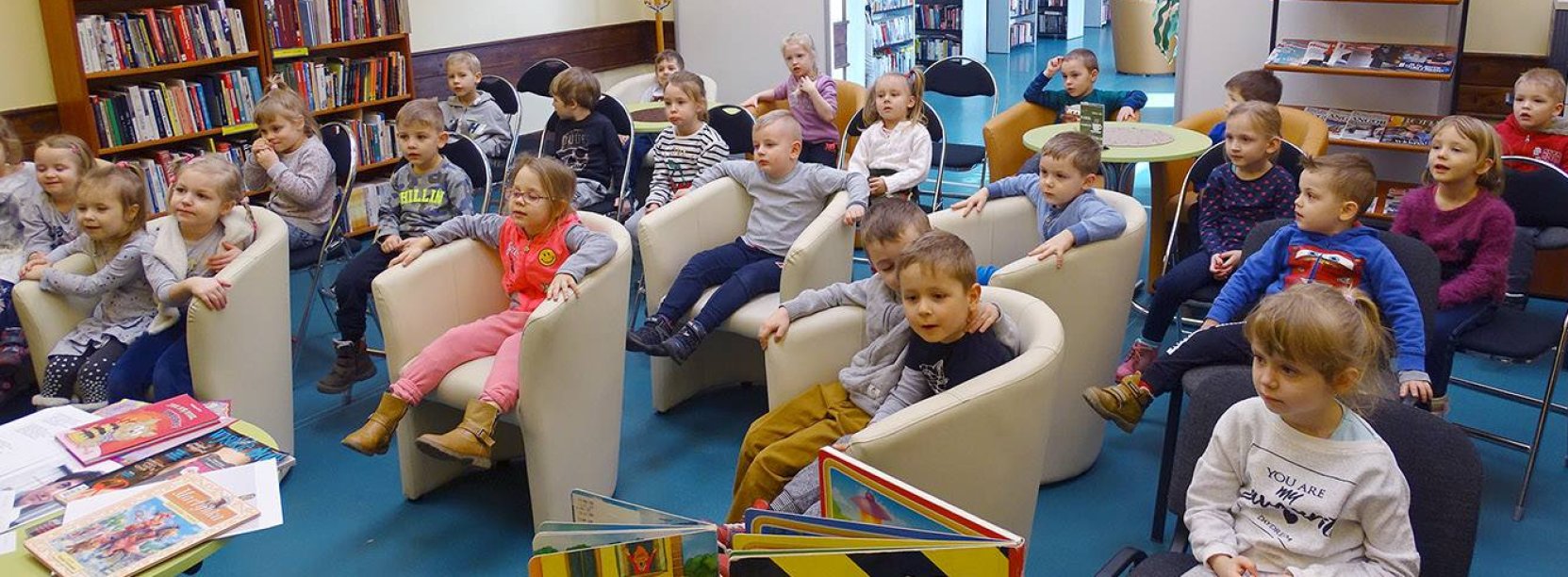 Przedszkolaki siedzące w fotelach w pomieszczeniu biblioteki, na pierwszym planie książki