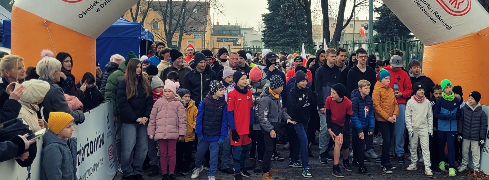 Kilkadziesiąt osób w róznym wieku na starcie wyścigu, u góry napis Dzierżoniów Nastraja Pozytywnie