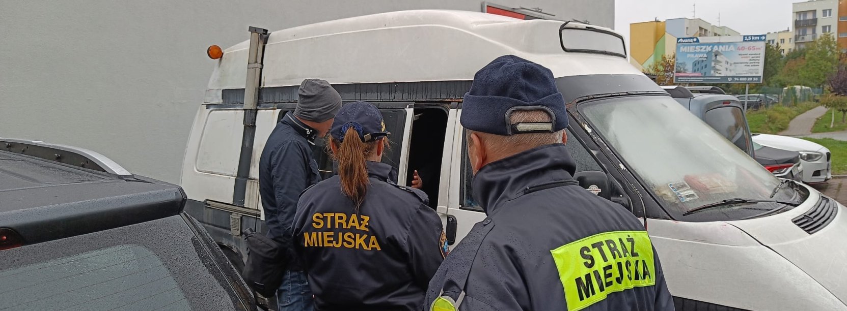 Strażnicy miejscy i kierowca przy białym busie