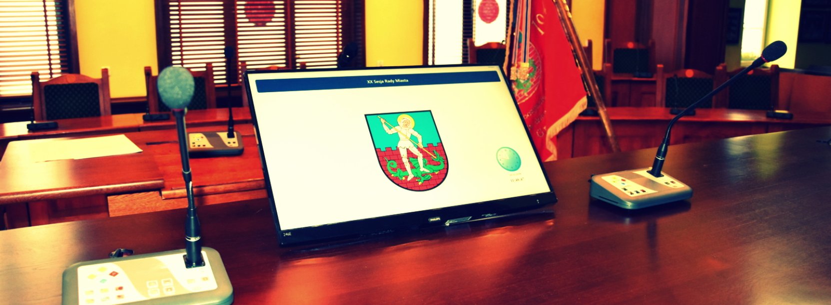 Sala obrad radnych, stół prezydialny, na stole monitor z herbem Dzierżoniowa i mikrofony