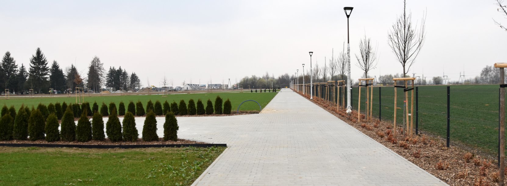 Ogordzony, pokryty trawą teren cmentarza i długa aleja z kostki betonowej