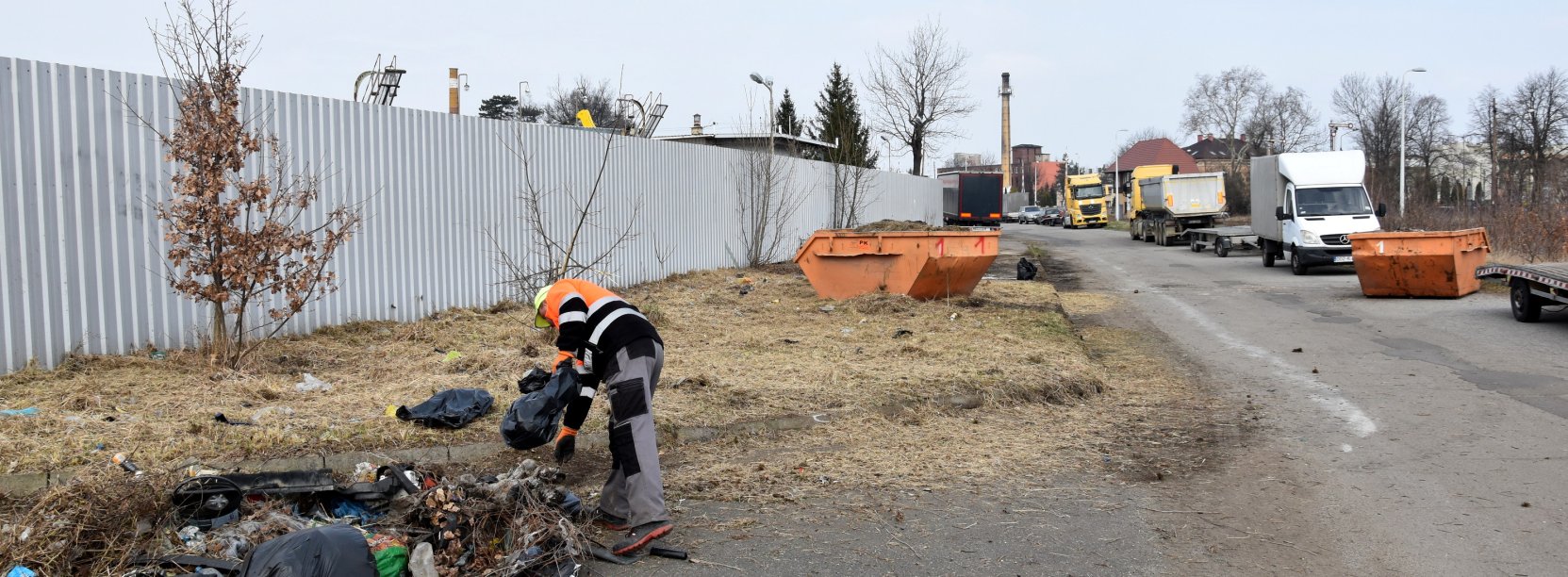 Mężczyzna w pomarańczowej kamizelce sprzątający śmieci porzucone koło drogi