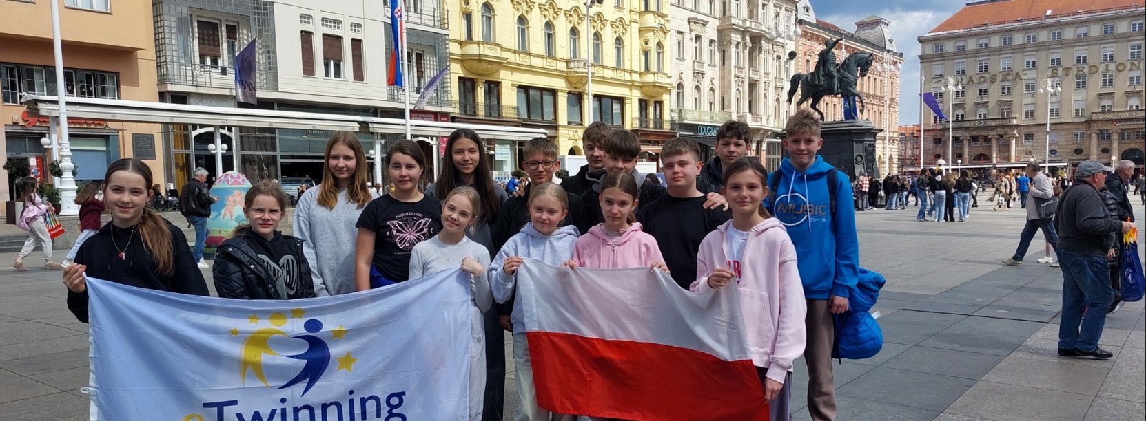 Grupa uczniów SP9 na rynku w stolicy Chorwacji. Cześć uczniów trzyma dużą flagę Polski