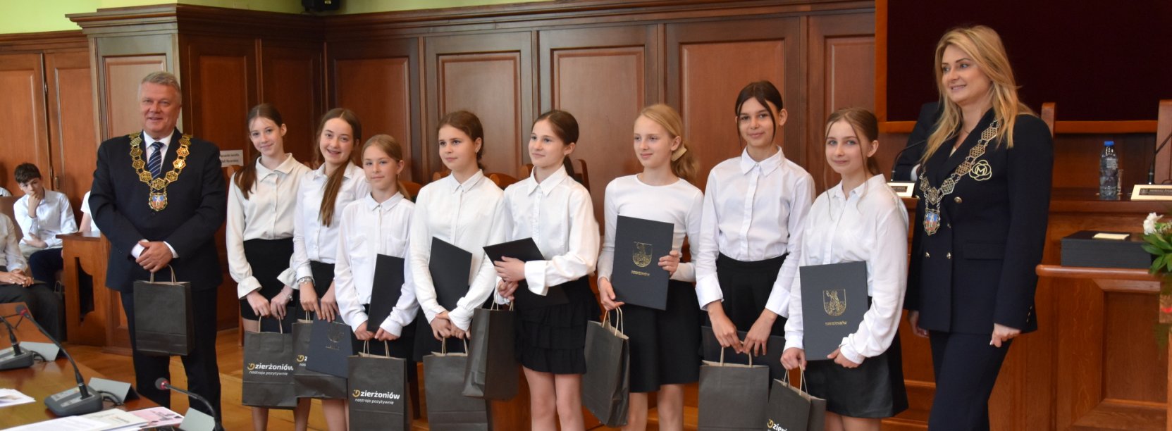 Uczennice w białych koszulach z dyplomami w rękach, obok burmsitrz i przewodnicząca Rady Miejskiej Dzierżoniowa