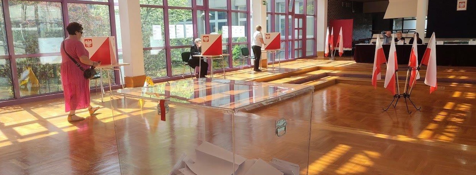 Lokal wyborczy z urną, stolikami do głosowania i flagami Polski