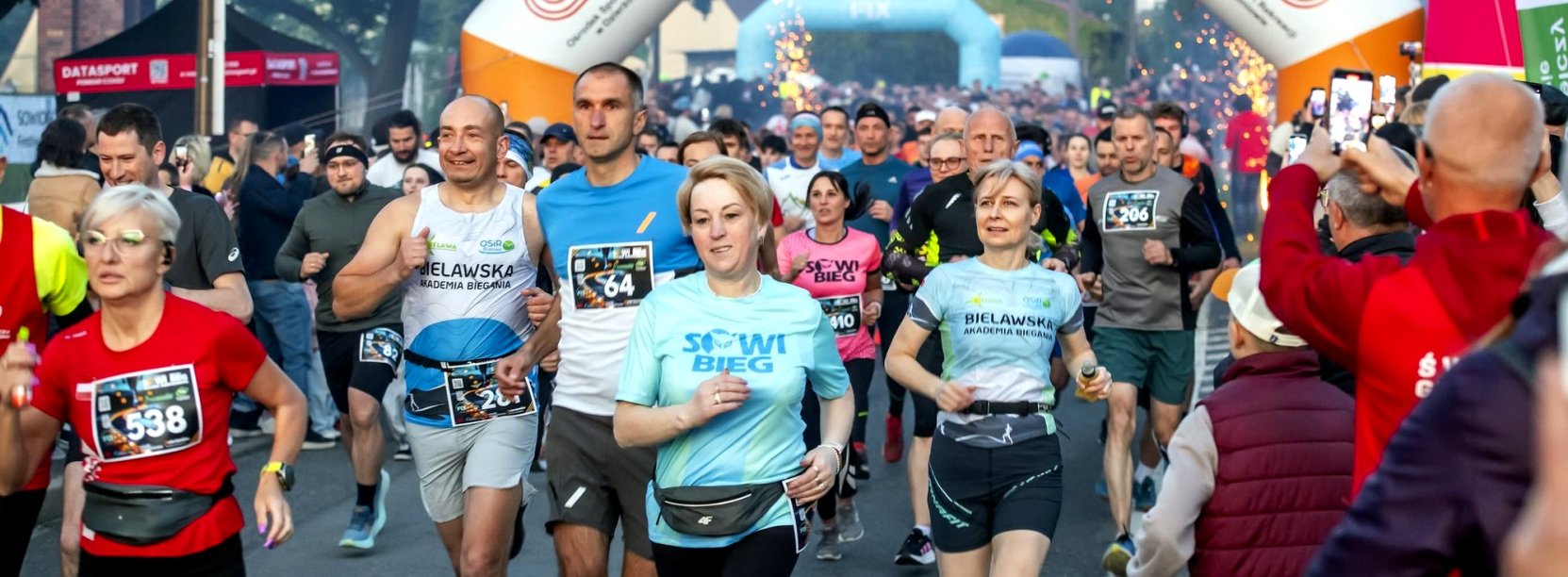 Ulica zapełniona biegaczami w sportowych strojach, za nimi napis Dzierżoniów