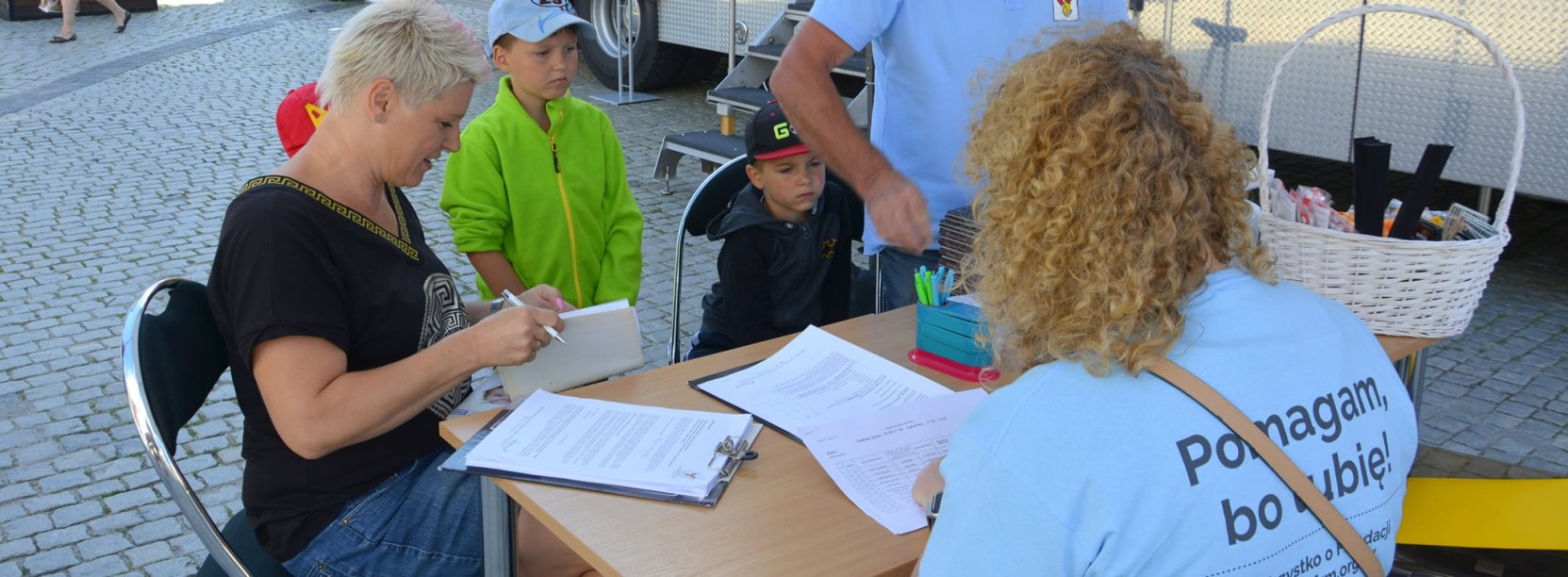 Rejestracja przed ambulansem fundacji Ronalda McDonalda w dzierżoniowskim Rynku, Kobieta i mężczyzna z dziećmi są przyjmowani w rejestracji