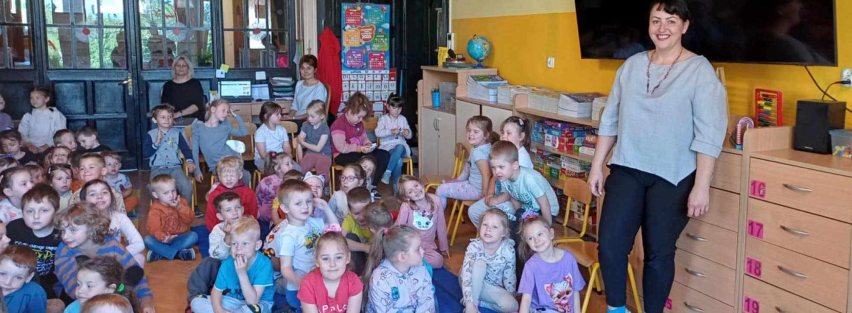 Grupa przedszkolaków siedzących na podłodze w dużym pomieszczeniu