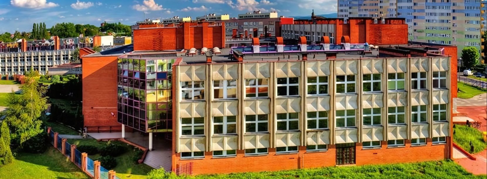Duży budynek SP 1 z betonu i czerwonej cegły, w tle osiedle mieszkaniowe