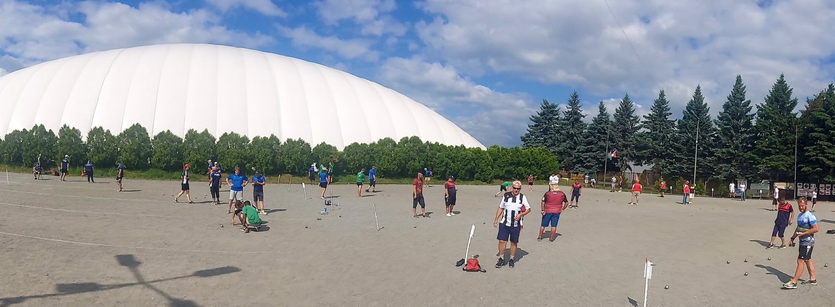 Duży plac, ludzie grający grupkami w petanque