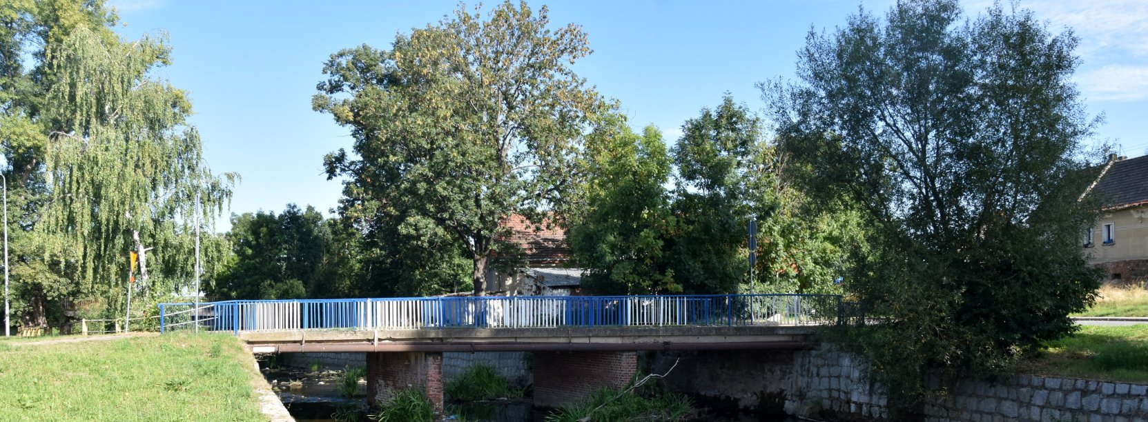 Most nad rzeką Piławą, po bokach i za mostem duże drzewa