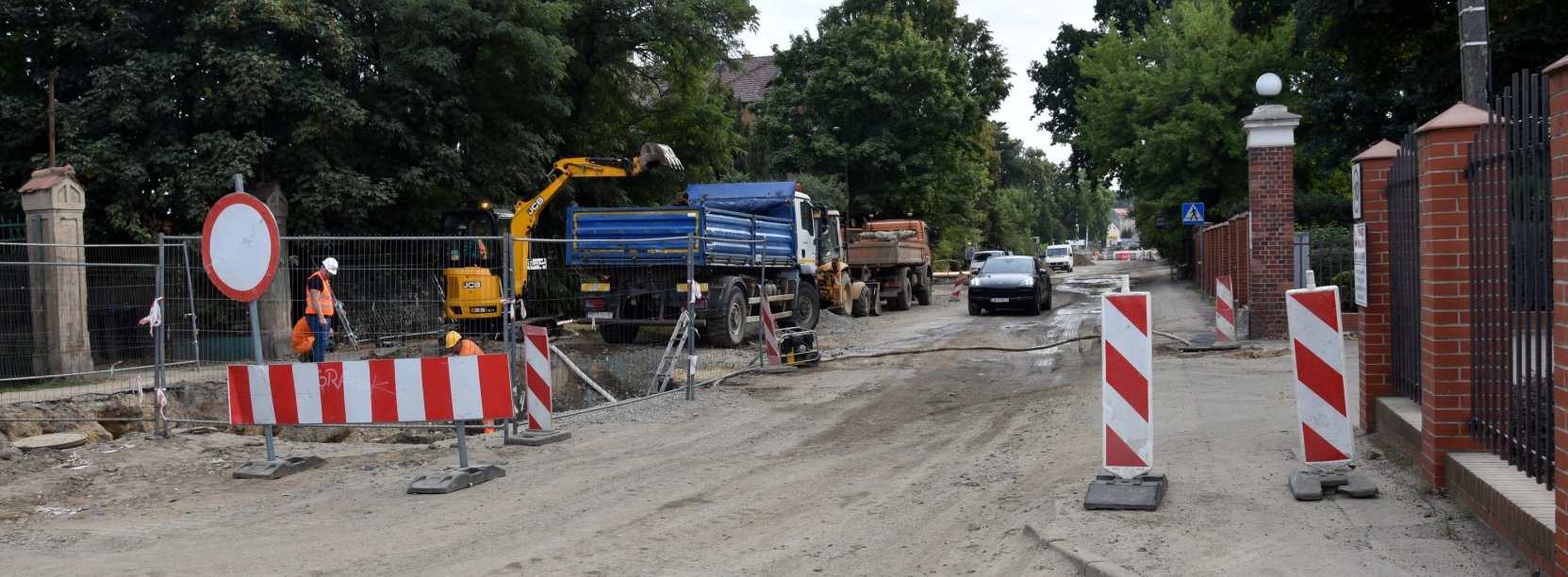 Droga miejska podczas remontu - pracująća koparka, obok samochód ciężarowy i pracownicy w pomarańczowych kamizelkach