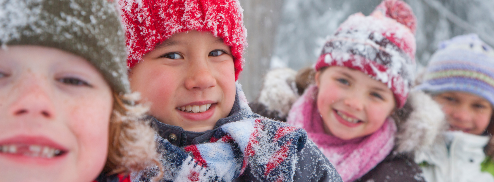 Czworo uśmiechniętych dzieci w zimowej scenerii, w ośnieżonych czapkach