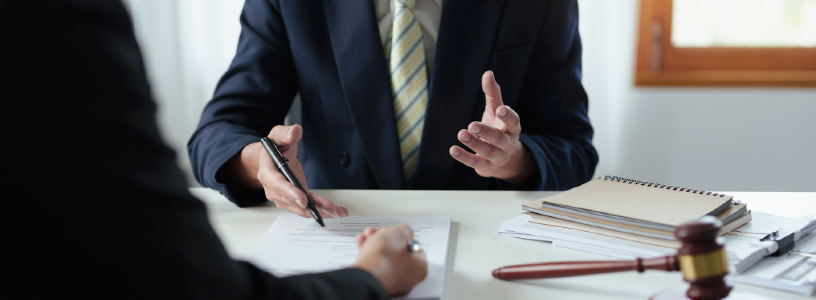 Mężczyzna w garniturze przy biurku, z dokumentami, tłumaczący coś drugiej osobie