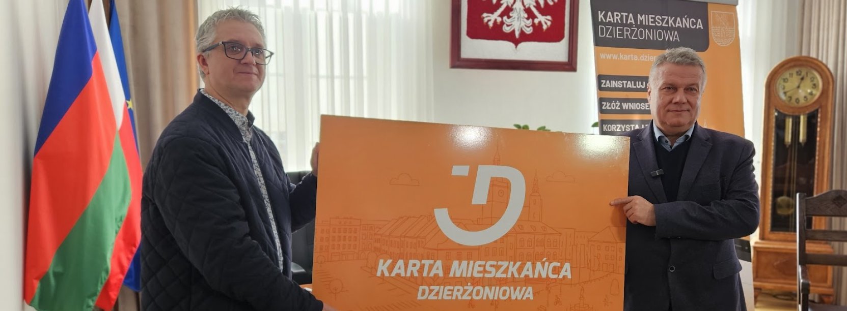 Mieszkaniec dzierzoniowa oraz burmistrz trzymają duża plastikową pomarańczową kartę meiszkańca