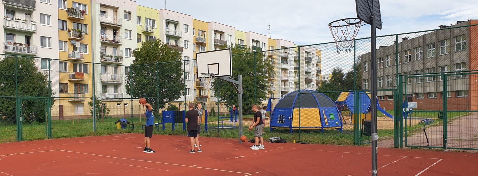 Czwórka chłopców na boisku do kosza, za nimi długi blok