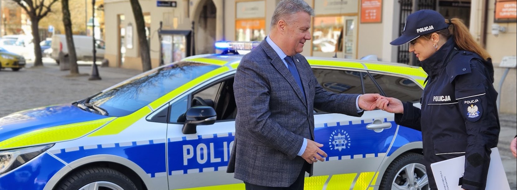 Burmistrz wręczający kluczyki policjantce, w tle nowy radiowóz