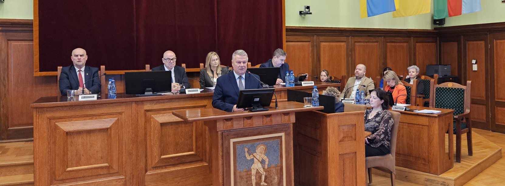 Burmistrz przy mównicy, za nim stół przy którym siedzi przewodnicząca i trzech wiceprzewodniczących