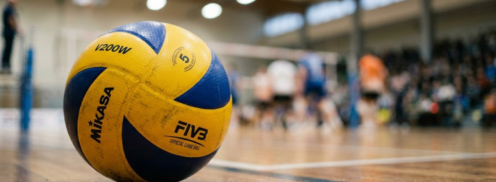 Piłka do siatkówki leżąca na parkiecie, w tle mecz siatkówki