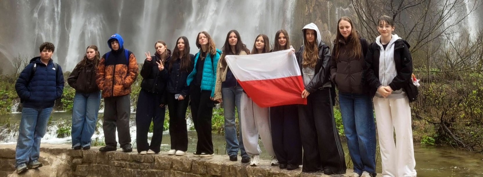 Uczniowie na wspólnym zdjęciu z flagą Polski, na drugim planie wodospad