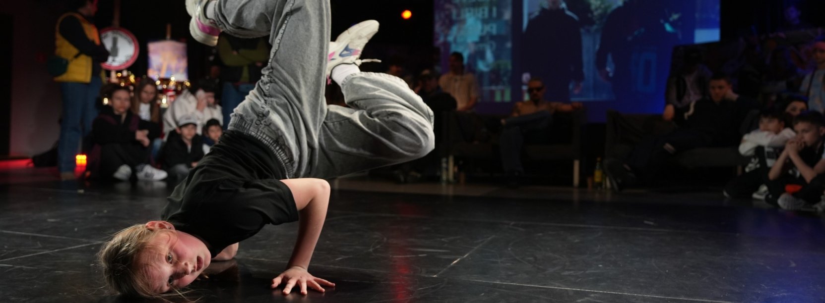 Dziewczyna tańczy będąc głową w dół, za nią widzowie