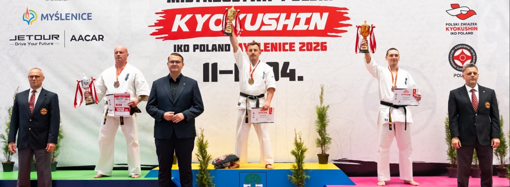 Trzech karateków na podium, Tomasz Staściuk na pierwszym miejscu z uniesionym w górę pucharem 