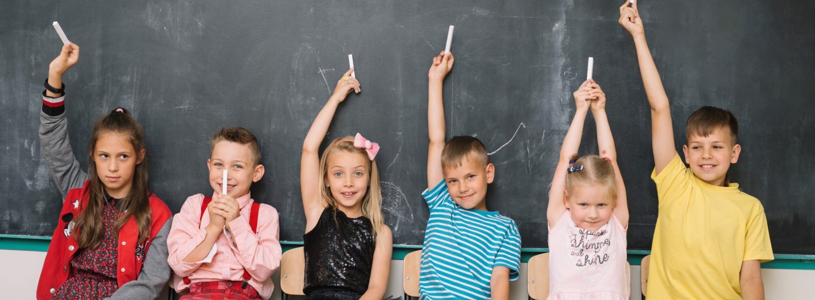 Trzech chłopców i trzy dziewczynki siedzą na krzesłach, za nimi tablica szkolna