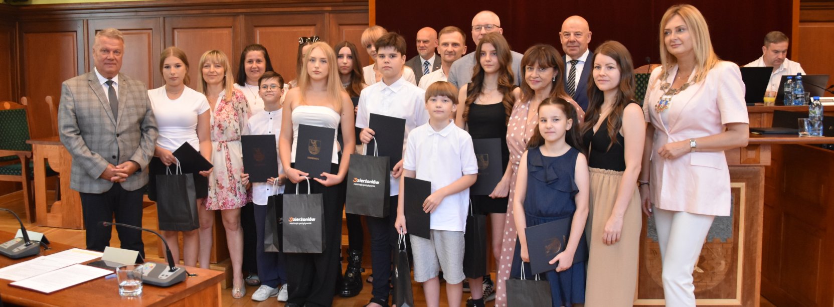 Kilkunastu uczniów z dyplomami w dłoniach, obok burmistrz i przewodnicząca rady