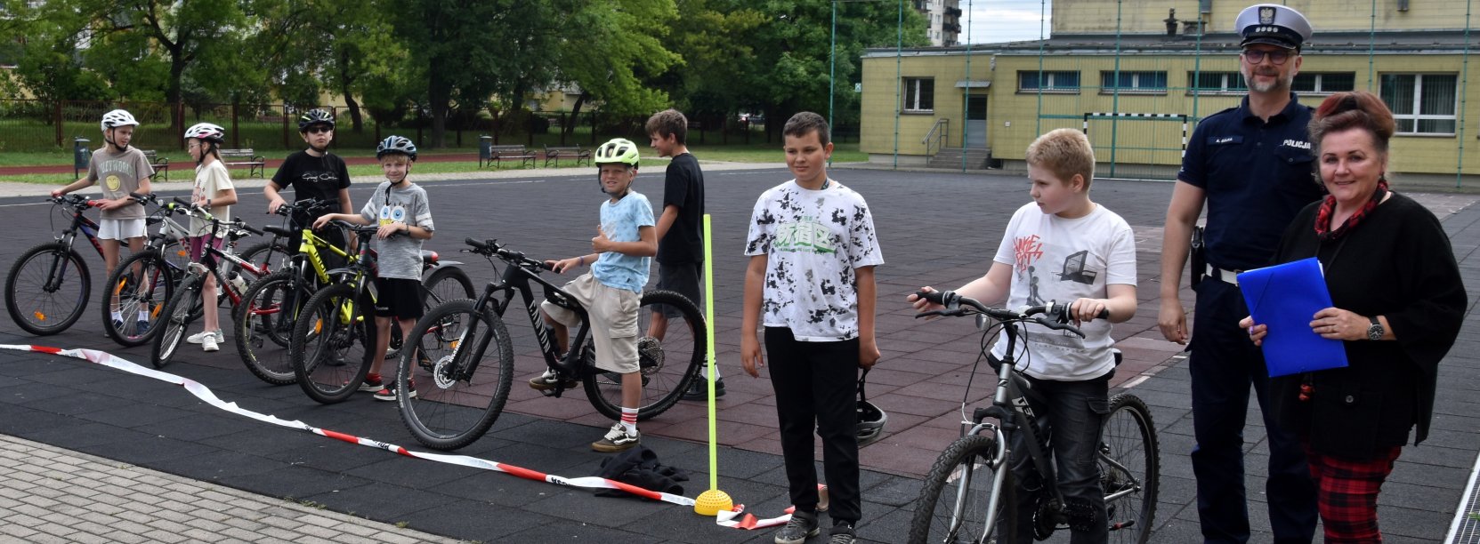 Grupa uczniów z rowerami ustawiona w szeregu, obok policjant i nauczycielka