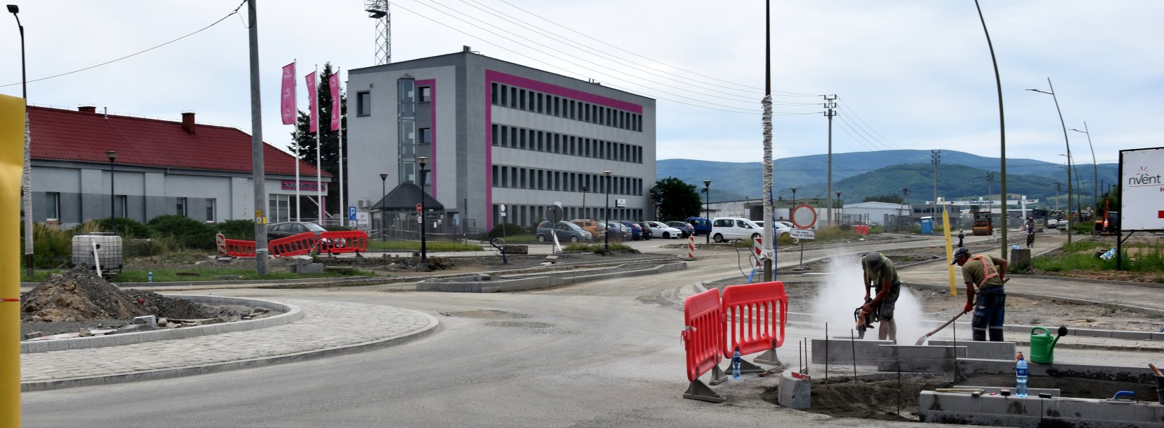 Rondo i droga w budowie, przy rondzie pracownicy w tle niewielki biurowiec