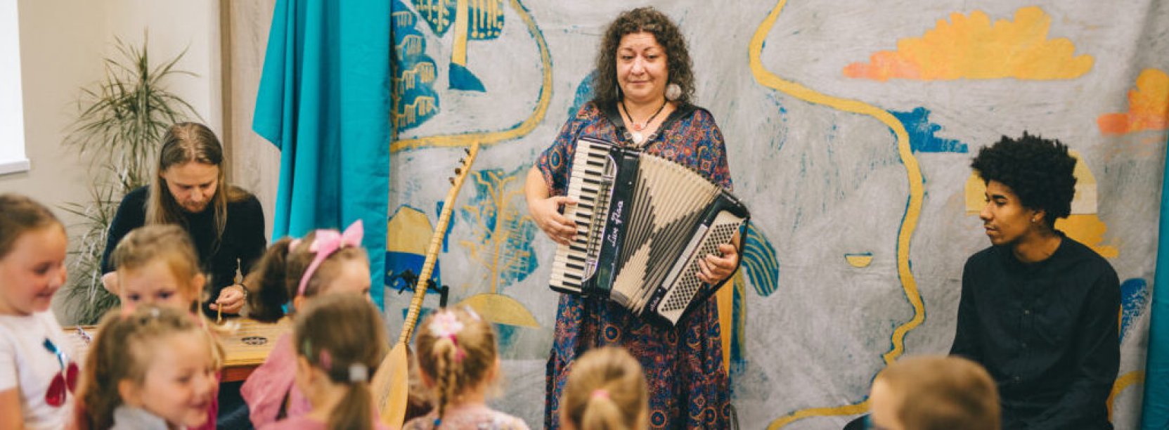 Kobieta grająca na harmonii, przed nią grupa dzieci