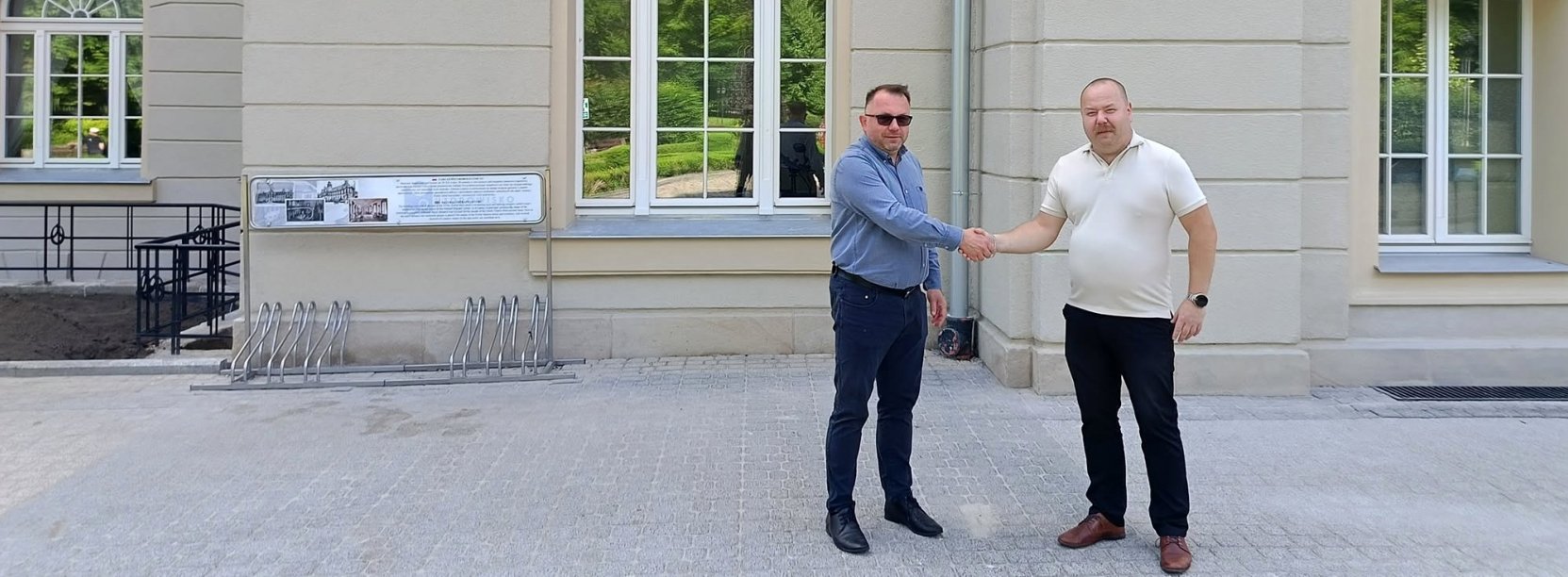 Prezes uzdrowiska i zastępca burmistrza ściskają sobie dłonie, w tle budynek