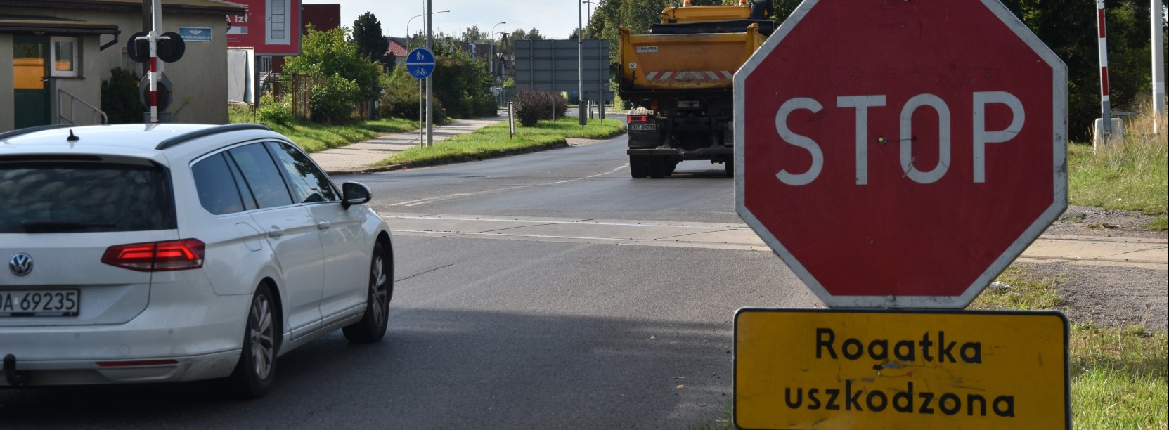Biały samochód przed przejazdem kolejowym, po prawej znak "Stop"