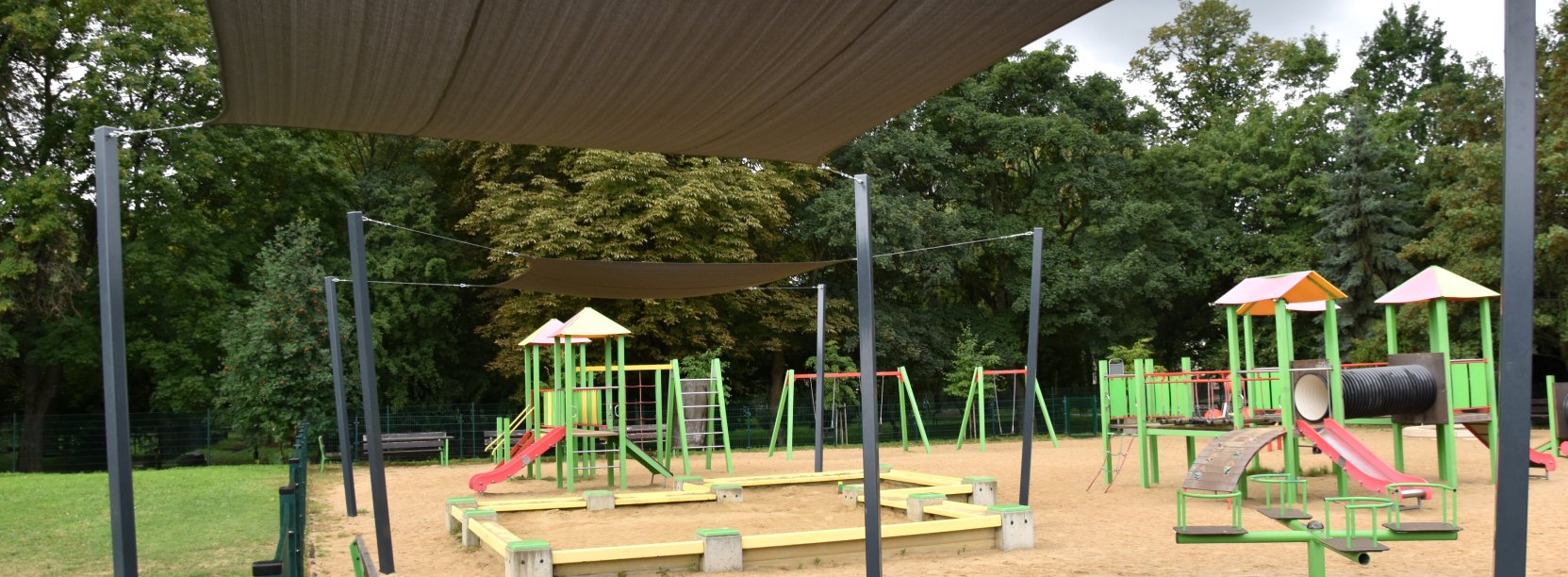 Plac zabaw z piaskowym podłożem, urządzeniami do zabawy i żaglami dającymi cień