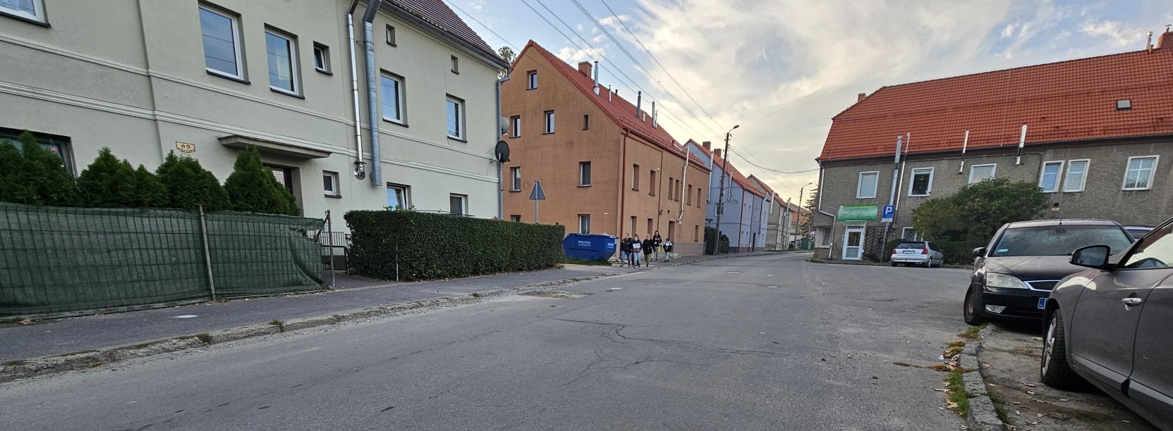 Droga asfaltowa, po bokach domy, chodnikiem idzie grupka dzieci