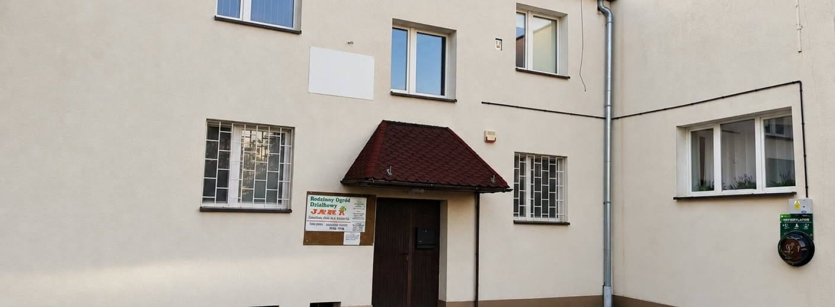 Dwupiętrowy budynek, przy wejściu zamontowany zewnętrzny defibrylator