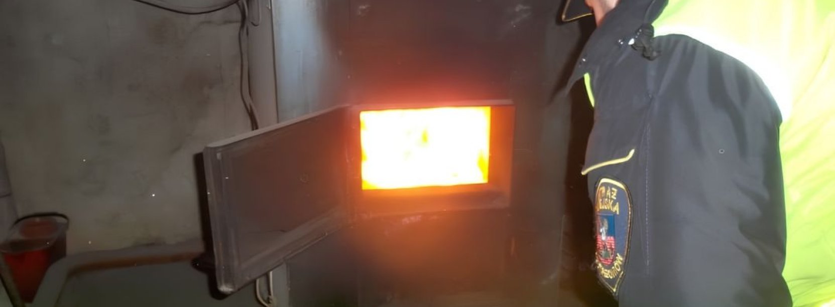 Strażnik miejski w żółtej kamizelce zaglądający do wnętrza pieca