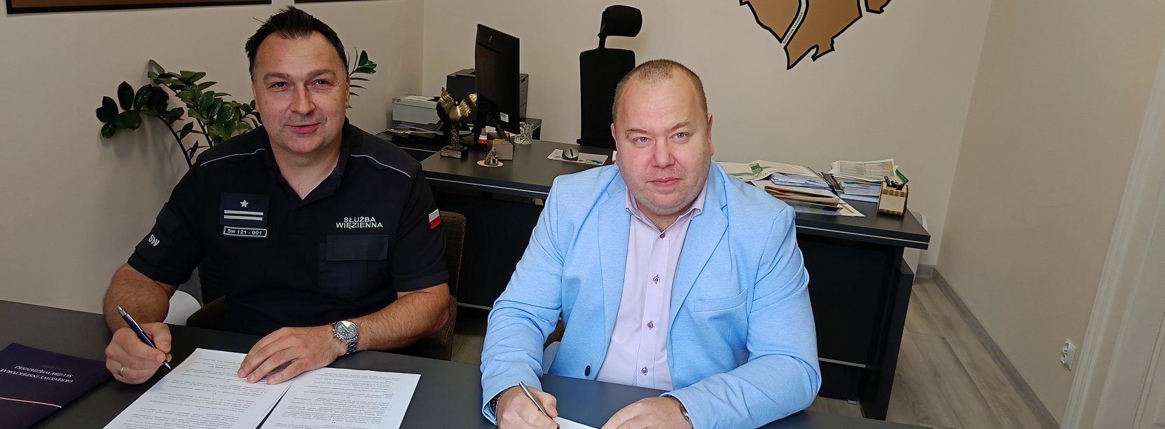 Zastępca burmistrza i komendant aresztu przy biurku podpisują porozumienie