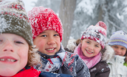 Czworo uśmiechniętych dzieci w zimowej scenerii, w ośnieżonych czapkach